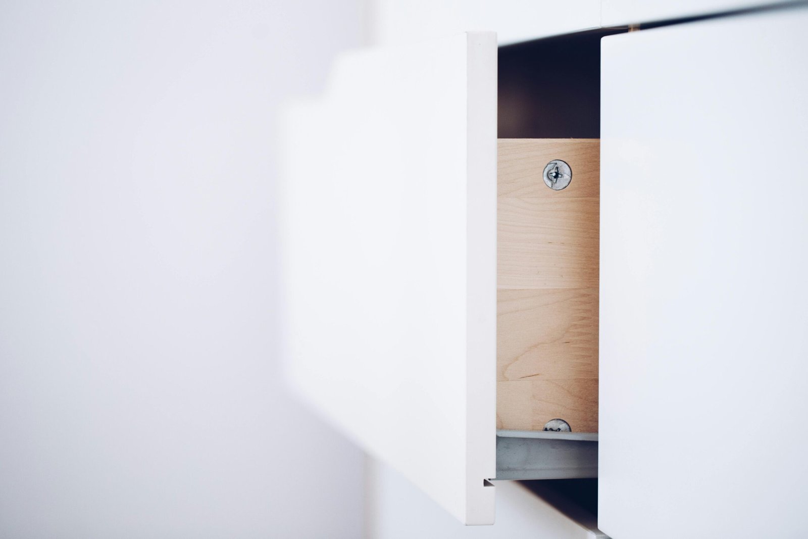 Close-up of an open white drawer revealing a wooden interior and screws in a minimalist design.