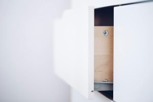 Close-up of an open white drawer revealing a wooden interior and screws in a minimalist design.